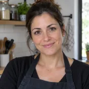 Donna sorridente con capelli castani raccolti e grembiule scuro in una cucina luminosa